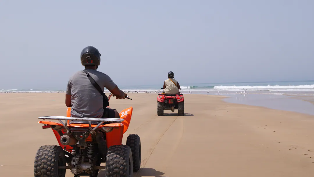 Quad bikes ride along a wide beach toward the sea.