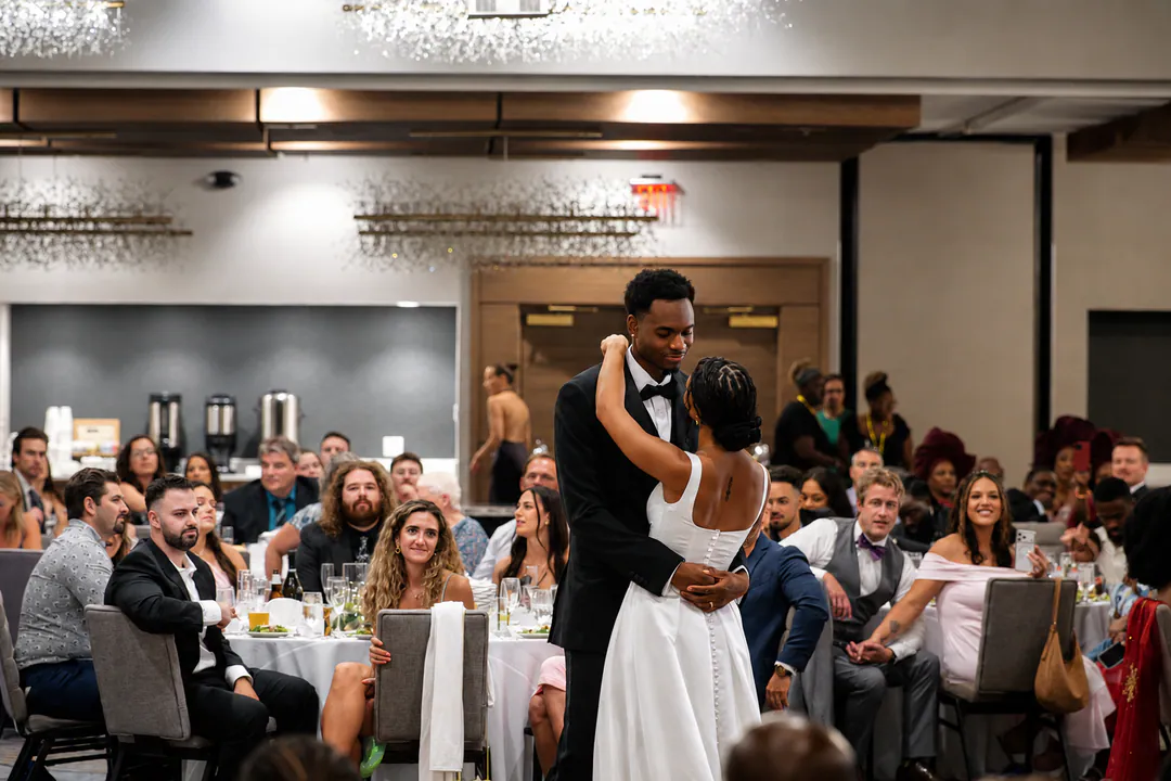 A couple shares their first dance at a wedding reception while guests watch from their tables.
