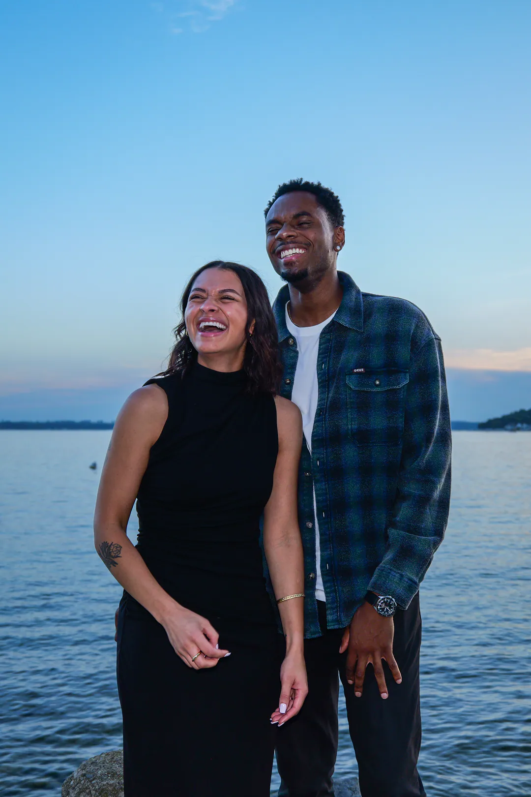 A couple laughs together by the water at dusk.